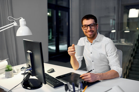business, graphic design and technology concept - smiling businessman or designer with computer and pen tablet drinking coffee at dark night office