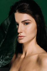 beautiful girl with perfect skin posing with palm leaf isolated on green