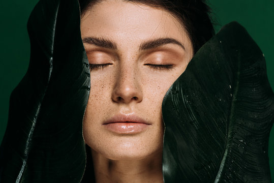 Portrait Of Beautiful Girl With Closed Eyes Posing With Green Leaves Isolated On Green