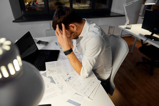 business, deadline and stress concept - stressed businessman with papers and laptop computer working at night office