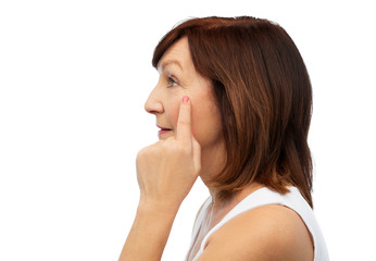 beauty, skin aging and old people concept - profile of senior woman pointing to her eye wrinkles over white background