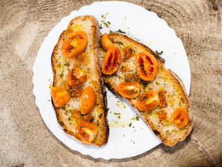 grilled bread with Italian tomatoes, orange color, very long lasting, seasoned with olive oil and oregano, for a healthy breakfast, shot from above, on a wooden surface