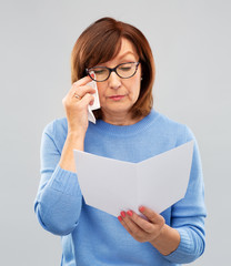 sorrow, bad news and old people concept - sad senior woman in glasses reading letter and crying over grey background