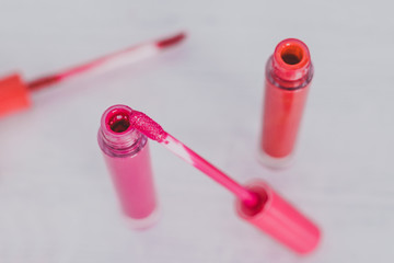 close-up of pink and orange lipglosses or liquid lipsticks on light wooden table