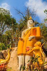 Yellow big Buddha on the stair way to the hill at Wat Khao Rup Chang or Temple of the Elephant Hill, one of the most famous attractions in Phichit province, Thailand. © kampwit