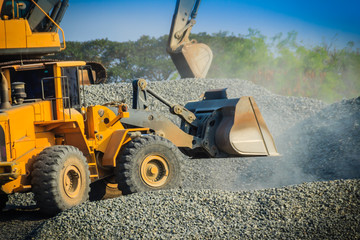 Obraz na płótnie Canvas Yellow wheel loader bulldozer is working in quarry against the background of crushed stone storage.