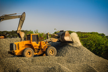 Yellow wheel loader and excavator are working in quarry against the background of crushed stone storage.