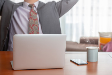 Businessman gesturing while working on a wooden table with a laptop a mobile and a mug of infusion