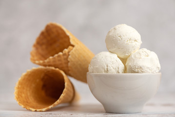 Fototapeta na wymiar Bowl of vanilla ice cream and waffle cones on light background. Side view