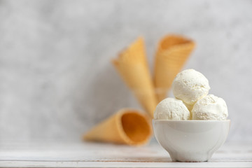 Bowl of vanilla ice cream and waffle cones on light background. Side view. With copy space