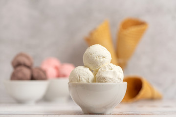 Bowl of vanilla, chocolate and pink berries ice cream and waffle cones on light background. Side view