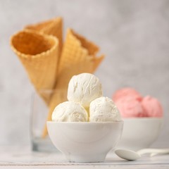 Bowl of vanilla and pink berries ice cream and waffle cones on light background. Side view