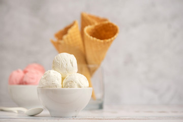 Bowl of vanilla and pink berries ice cream and waffle cones on light background. Side view. With copy space