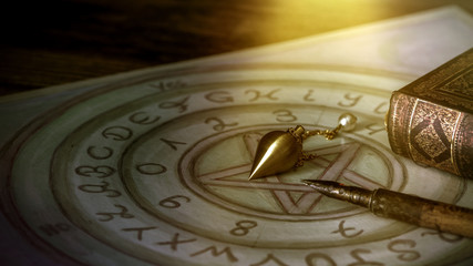Pendel, Feder und altes Buch auf einem Ouijabrett mit Pentagramm