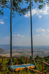 Wooden swing is hanged on tree branch with blue sky and white clouds background.