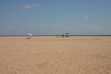 Fototapeta premium Spacious lonely beach by the sea. Only three tourists rest under their umbrellas in the distance. There is a boat in the sea.