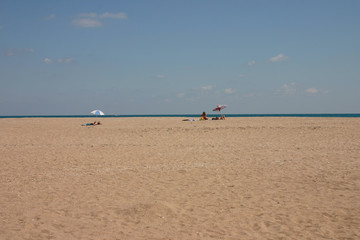 Spacious lonely beach by the sea. Only three tourists rest under their umbrellas in the distance. There is a boat in the sea.