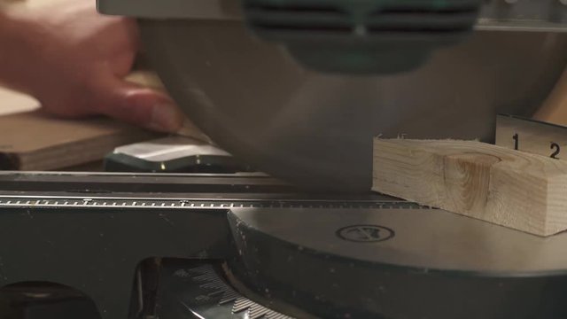 A side view of a miter saw cutting a work piece at a selected angle. Carpenter is taking cut work piece
