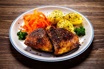 Grilled thighs with boiled potatoes and vegetable salad on wooden table