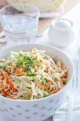 Fresh cabbage salad with carrots and cucumber in a white bowl, selective focus
