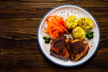 Grilled thighs with boiled potatoes and vegetable salad on wooden table