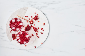 Fresh pomegranate juice with ice and red pomegranate seeds on white marble serving plate over marble background. Top view with copy space for text. Overhead shot.