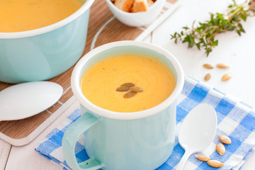 Obraz na płótnie Canvas Pumpkin soup in blue enamelled mug with pumpkin seeds, horizontal