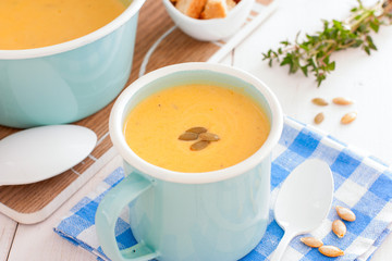Pumpkin soup in blue enamelled mug with pumpkin seeds, horizontal