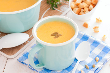 Pumpkin soup in blue enamelled mug with pumpkin seeds, horizontal