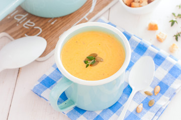 Pumpkin soup in blue enamelled mug with pumpkin seeds, horizontal
