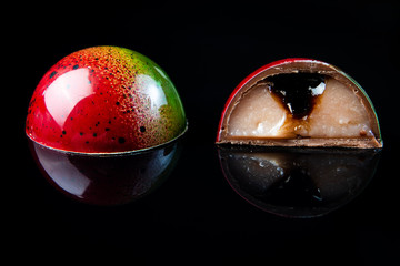 Colorful chocolate candy in a cut on the black glossy background with reflection