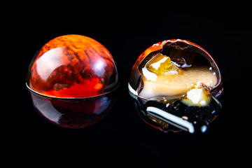 Colorful chocolate candy in a cut on the black glossy background with reflection