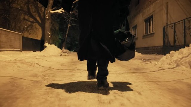 Bottom angle: Man ib black cloak walking through alley