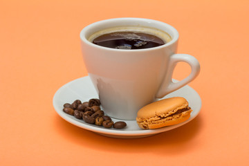 Cup of coffee with coffee beans and delicious macaron cake on peach background.
