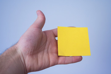 Empty yellow sticky note in human fingers. Blank in hand on gray background