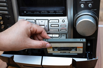 Women hand putting cassette into old fashioned audio tape player on top desk wood background
