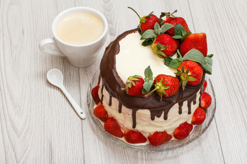 Homemade chocolate cake decorated with fresh strawberries on glass plate and cup of coffee on gray background.