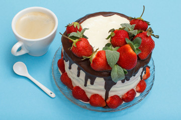 Homemade chocolate cake decorated with fresh strawberries on glass plate and cup of coffee on blue background.