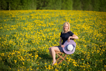 beautiful blonde woman is sitting on a wooden chair with blooming dandelion