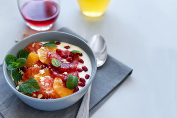 Bowl of homemade granola with yogurt, citrus and pomegranate seeds on gray wooden background. Selective focus. Healthy eating or vegetarian food concept