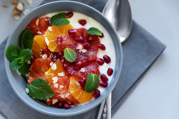 Bowl of homemade granola with yogurt, citrus and pomegranate seeds on gray wooden background. Selective focus. Healthy eating or vegetarian food concept