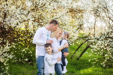 Naklejka na ściany i meble Happy parents mom and dad, daughter and son, young family outdoors in spring against the background of blooming apple and cherry trees