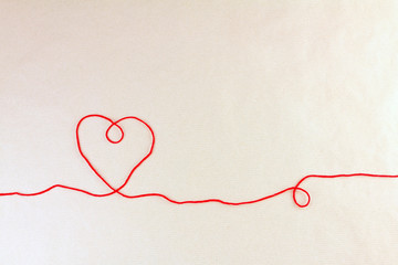 Red thread, heart and tangle on light craft paper background, top view