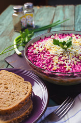 Traditional Russian herring under a fur coat in transparent plate with parsley. Rustic style.