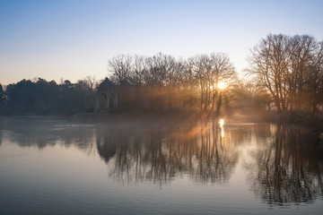 Fototapeta premium Tiefstehende Sonne und Nebel im winterlichen Stadtpark von Magdeburg am Adolf Mittag See
