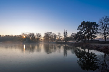 Fototapeta na wymiar Tiefstehende Sonne und Nebel im winterlichen Stadtpark von Magdeburg am Adolf Mittag See