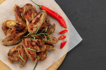 Baked chicken wings with and sweet chili sauce on  wooden board over dark background with copy space