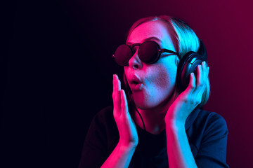 Surprised pretty woman with headphones listening to music over red neon background at studio.