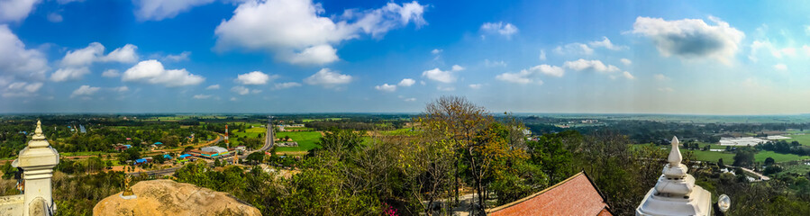 Fototapeta na wymiar Panorama view over highway from hilltop around with countryside green rice fields and blue sky background. The provincial highway with cars and trucks crossing the hills at Phichit province, Thailand.
