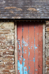 Red and distressed wooden door on an old stone barn with slate tiles